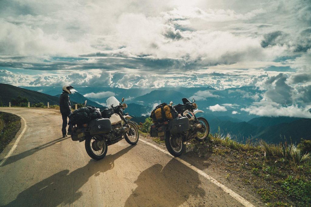 Two motorbikes on the side of a road, looking over a vista of mountains and clouds.